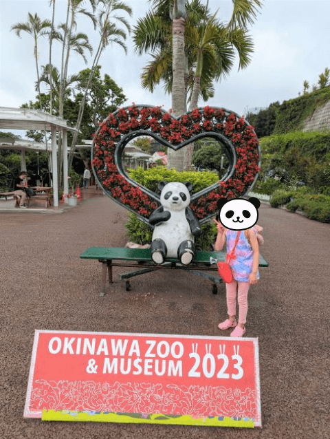 沖縄県沖縄市胡屋にある動物園「こどもの国沖縄ズージアム」のパンダの置物がいる写真スポットで6歳の女の子がピースサインをしている写真。OKINAWA ZOO ＆ MUSEUM2023と文字が入っている。