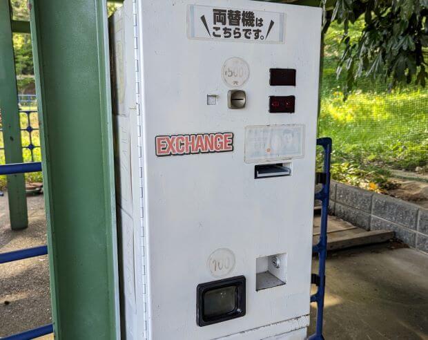 福岡県北九州市にある到津の森公園の園地ゾーン（遊園地）にある遊戯チケット（プレイチケット）販売機横に置いてある両替機の画像。