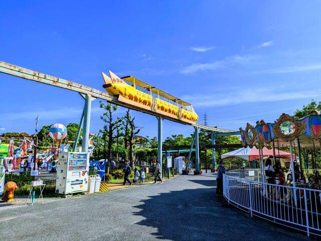 福岡県北九州市にある到津の森公園の園地ゾーン（遊園地）にあるミニモノレール、メリーゴーランドなどの乗り物と賑わう人たちの画像