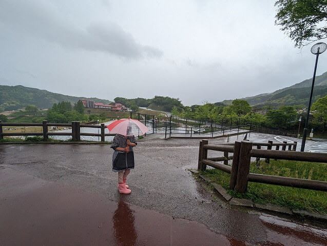福岡市南区にある「ABURAYAMA FUKUOKA」（旧油山牧場もーもーらんど・油山市民の森）の雨の日に女の子が傘をさして立っている画像