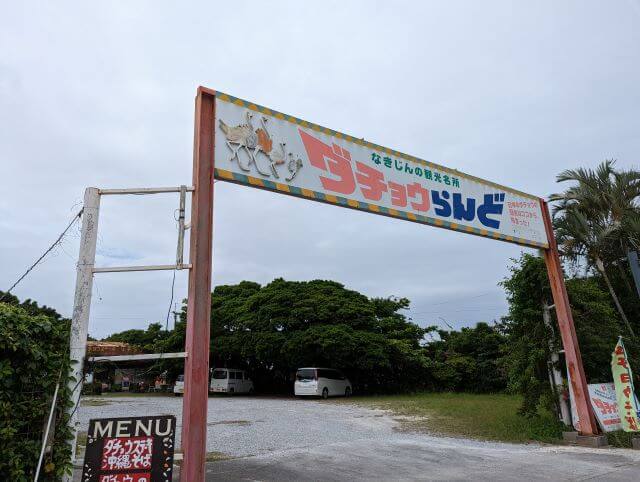 沖縄県国頭郡今帰仁村にある「だちょうランド沖縄」の入口の看板ゲートの画像。奥は駐車場。