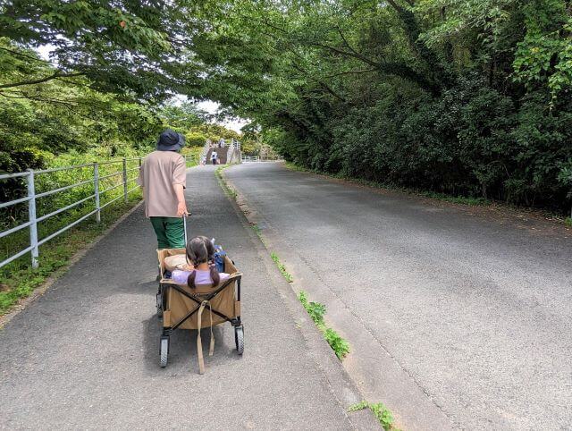 福岡県北九州市にある「響灘グリーンパーク」の駐車場の歩道でキャリーワゴンに乗っている女の子と引っ張っているお父さんの画像