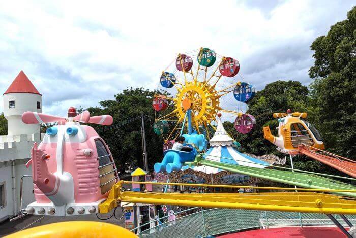 福岡市動物園の南園に位置する遊戯施設「ミニ遊園地」のアストロメリーに実際に乗って、回っているところを撮った画像。観覧車をバックに女の子がアストロメリーのゾウの乗り物に乗っている。