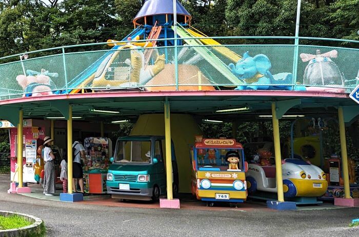 福岡市動物園の南園に位置する遊戯施設「ミニ遊園地」のアストロメリー下の13台の遊具の一部の画像。ちびまる子ちゃんのえんそくバスや車の乗り物が写っている。