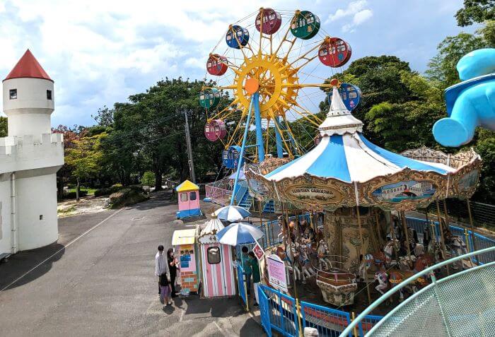 福岡市動物園の南園に位置する遊戯施設「ミニ遊園地」をアストロメリーに乗りながら撮った写真。観覧車とメリーゴーランドと来園者が写っている。