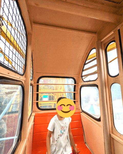 福岡市動物園の南園に位置する遊戯施設「ミニ遊園地」の観覧車の内部の画像。オレンジの椅子に女の子が腰かけている。